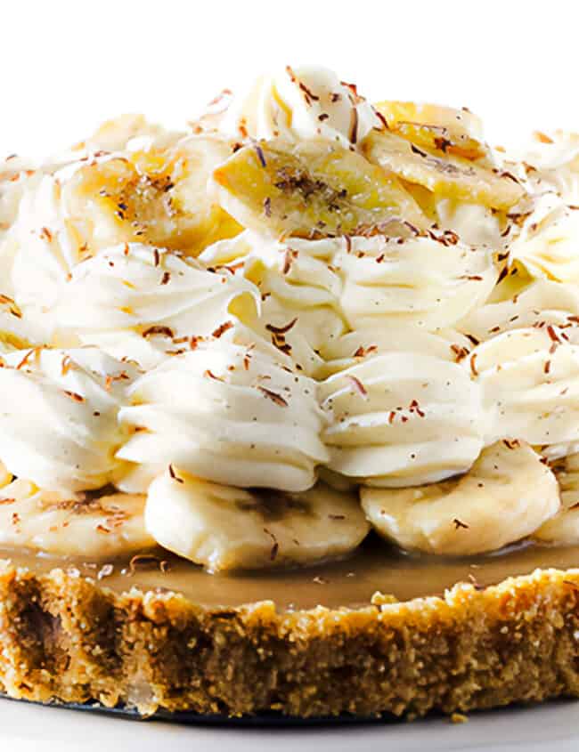 The Banoffee Pie on a cake stand showing the crust, caramel layer, banana layer, whipped cream and banana chips as decoration.