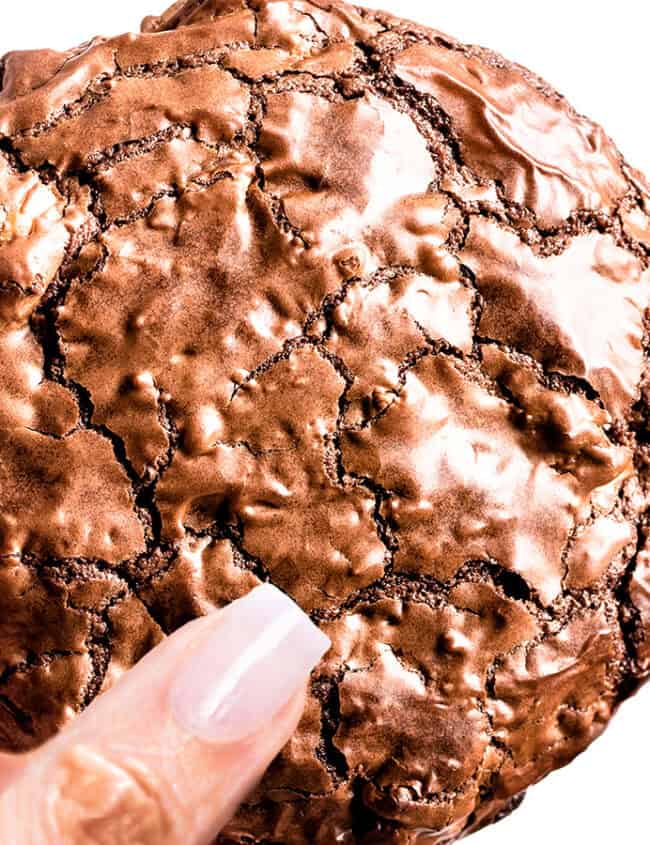 A woman's hand holding a shiny brownie cookie.