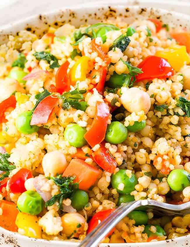 A close up image of Vegetable Moroccan Couscous in a bowl with a serving spoon.