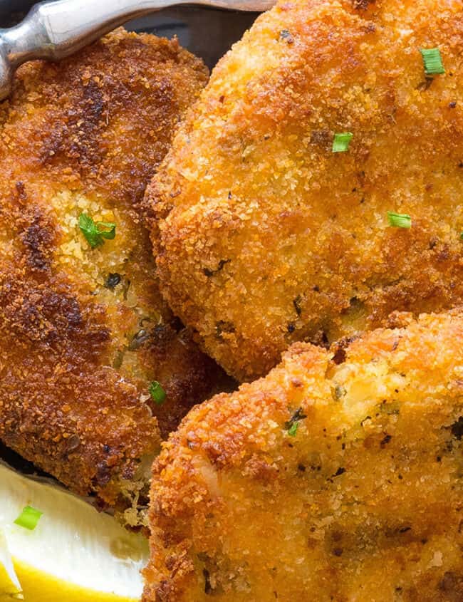 Three Crab Cakes on a plate with lemon wedges and a fork next to it.