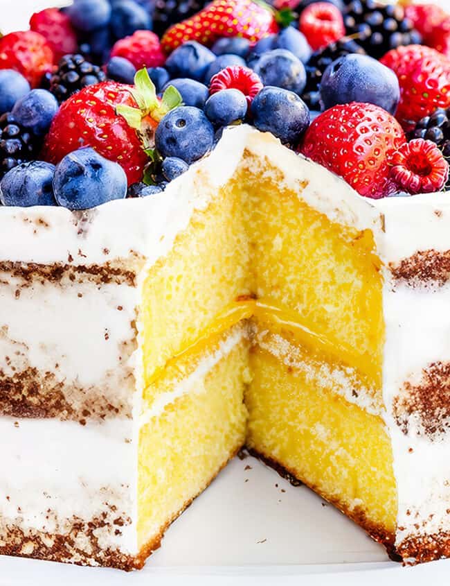 A lemon cake topped high with mixed berries with a slice cut out to reveal the lemon curd filling.