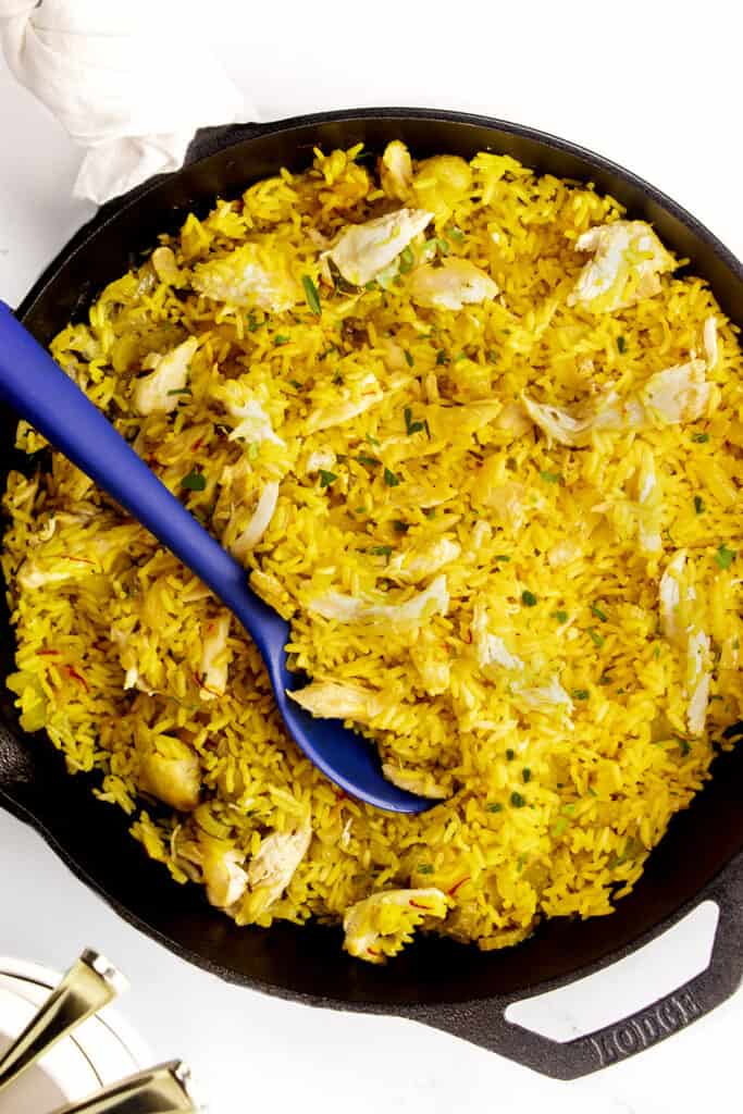 a pan full of Chicken and yellow rice in a black skillet.