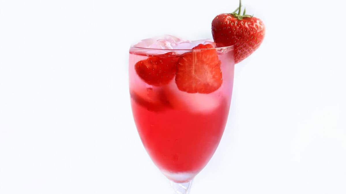 a close up image of a vibrant strawberry cocktail with a strawberry on the glass for garnish. 