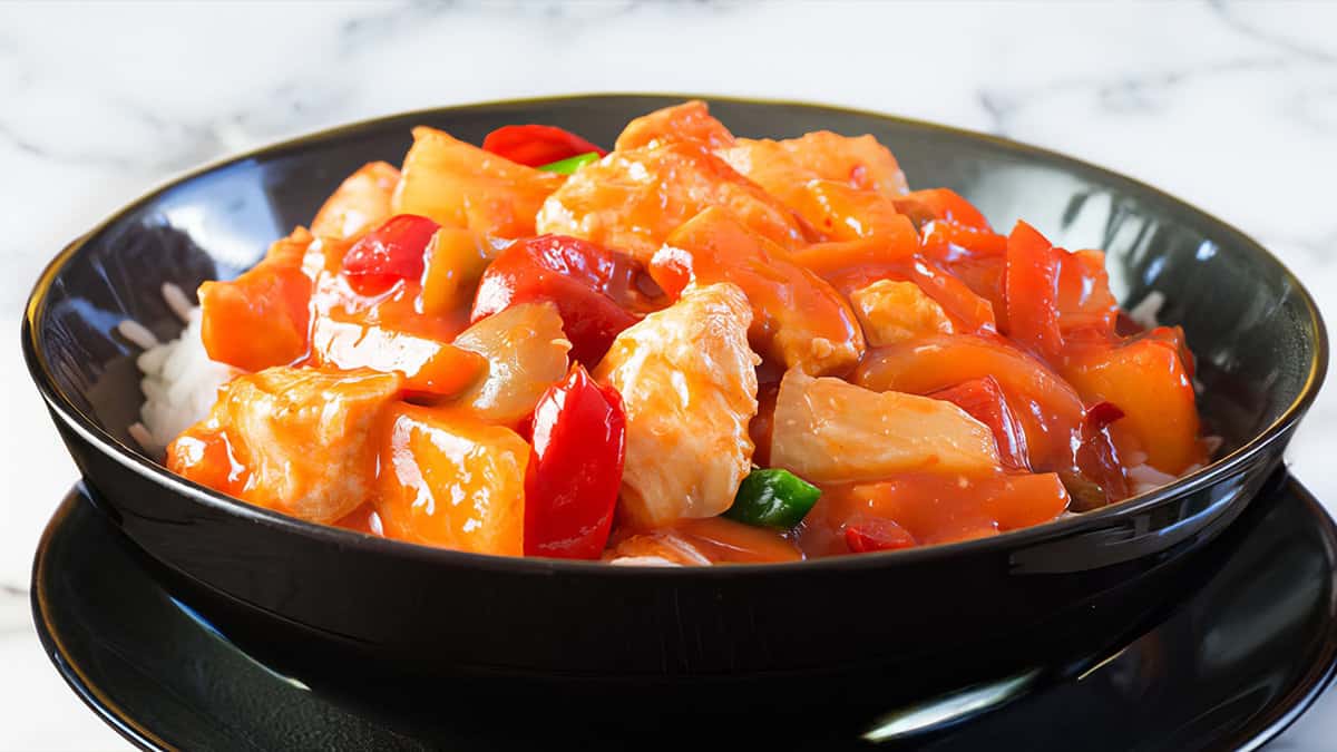 A close up image of a bowl full of Sweet and sour chicken over rice