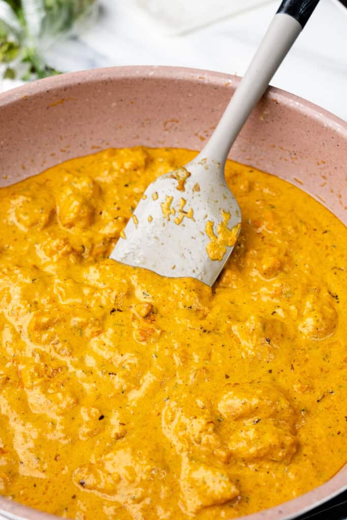 A vibrant image showing a pan of creamy butter chicken curry. The sauce, rich and orange in color.