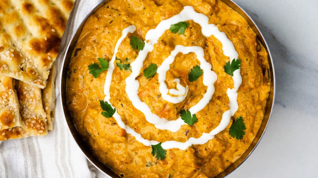 A bowl of vibrant orange color butter chick with a swirl of yogurt and fresh cilantro.