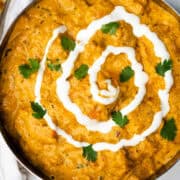 A bowl of vibrant orange color butter chick with a swirl of yogurt and fresh cilantro.