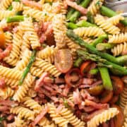 Close-up of a Bacon and Asparagus Pasta Salad with rotini pasta, asparagus, cherry tomatoes, bacon, and grated Parmesan cheese, all tossed in a light dressing, served in a large white bowl.