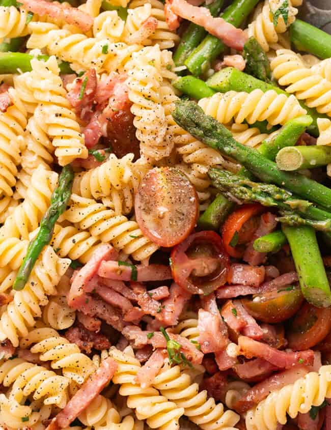 Close-up of a Bacon and Asparagus Pasta Salad with rotini pasta, asparagus, cherry tomatoes, bacon, and grated Parmesan cheese, all tossed in a light dressing, served in a large white bowl.