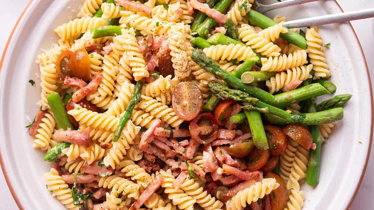 Close-up of a Bacon and Asparagus Pasta Salad with rotini pasta, asparagus, cherry tomatoes, bacon, and grated Parmesan cheese, all tossed in a light dressing, served in a large white bowl.