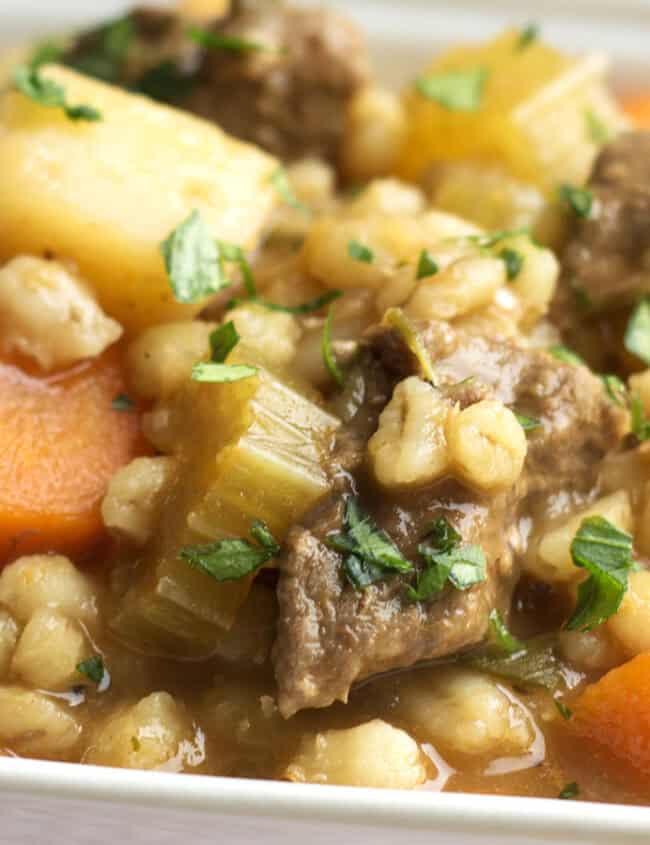 A square white bowl of beef and barley soup.