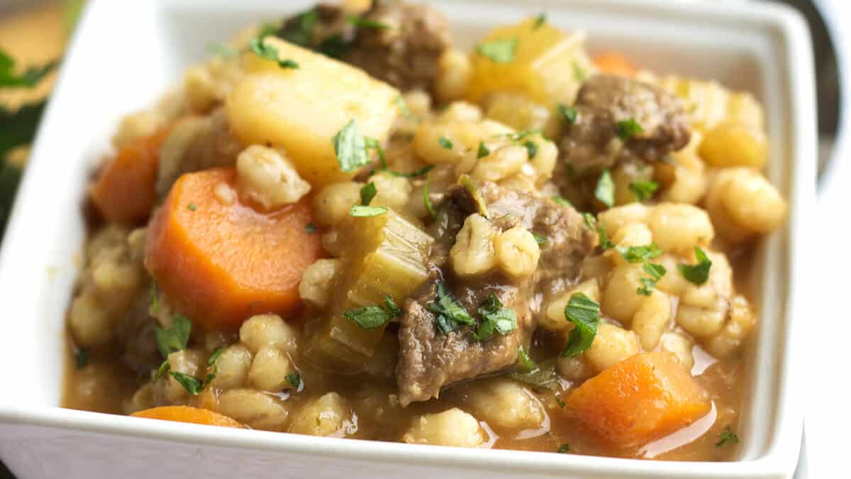 A square white bowl of beef and barley soup.