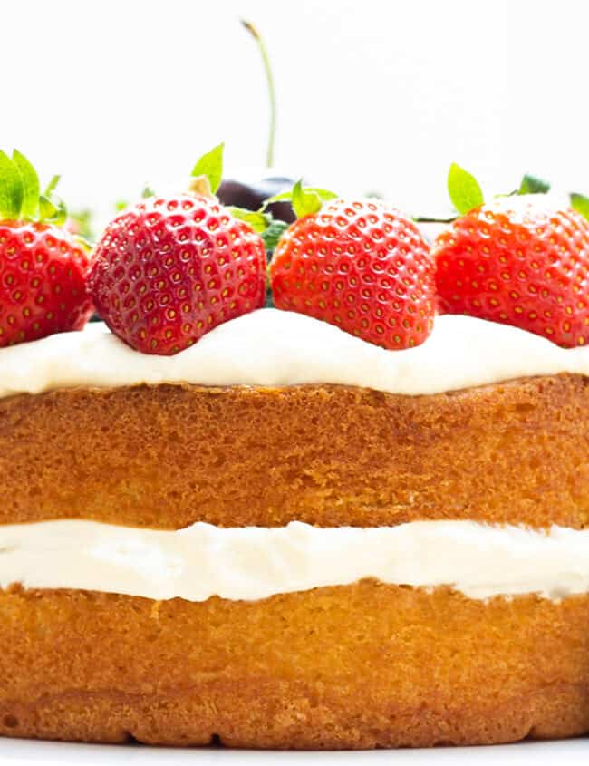 A layer cake on a cake stand topped with cream and fruit.