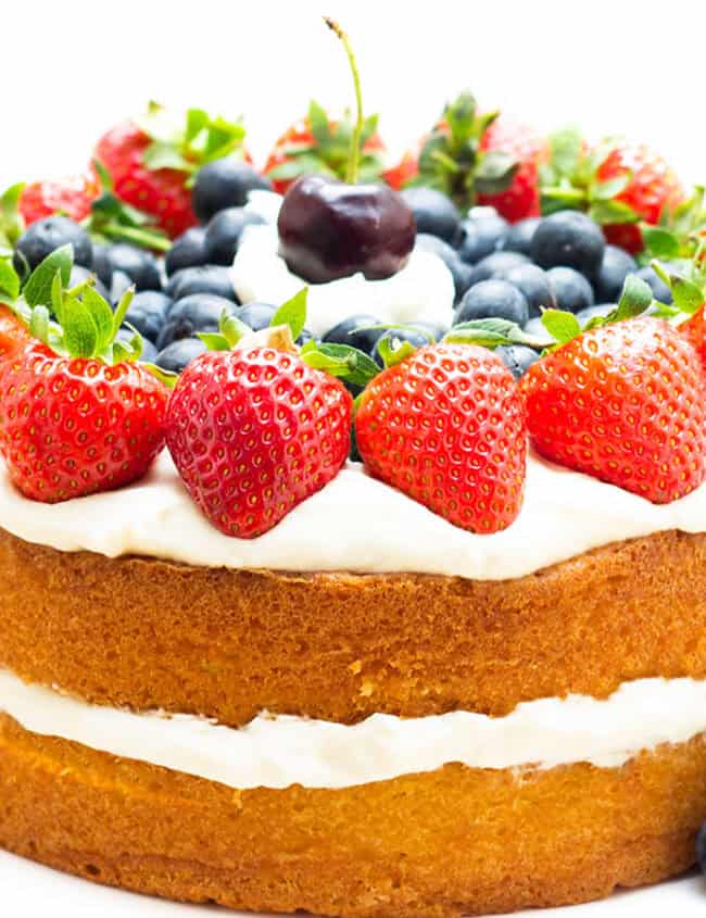 A layer cake on a cake stand topped with cream and fruit.