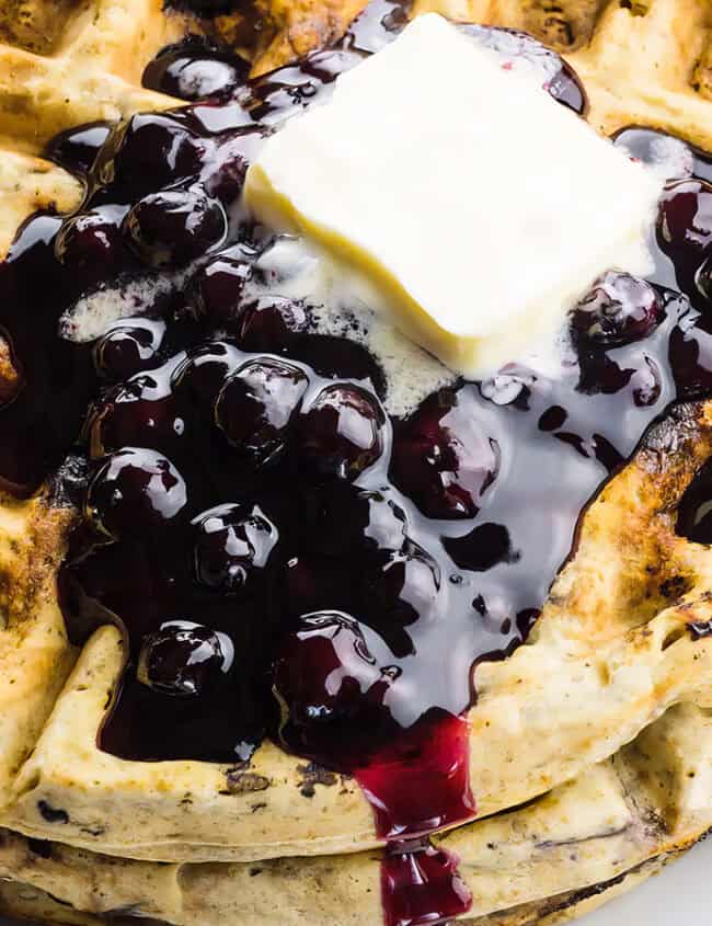 A close up image of Blueberry Waffles topped with butter and blueberry jam.