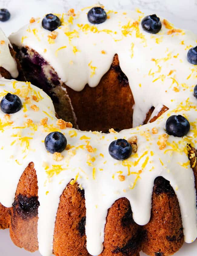 A lemon blueberry cake topped with white icing and blueberries.