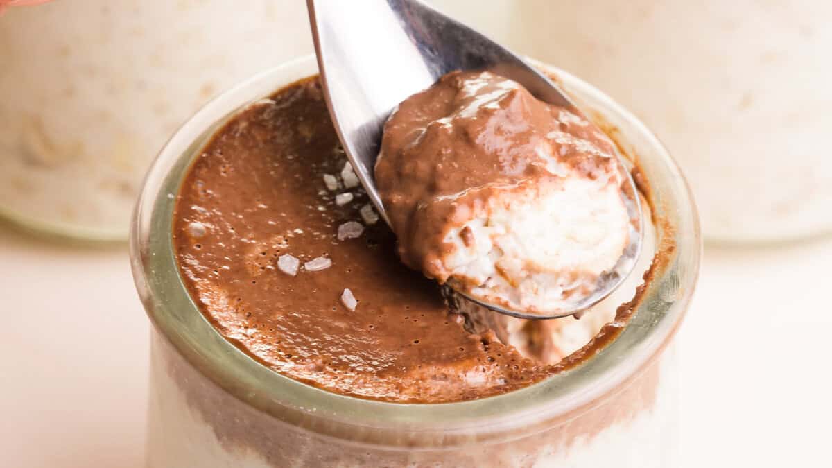 A clear jar filled with layered Bounty Overnight Oats, featuring a mix of rolled oats, chocolate shavings, and coconut flakes.