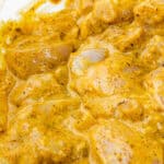 glass bowl filled with chunks of chicken marinating in a vibrant yellow sauce.