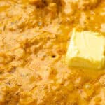 A vibrant yellow curry sauce with tender chicken pieces and a dollop of butter being melted in.