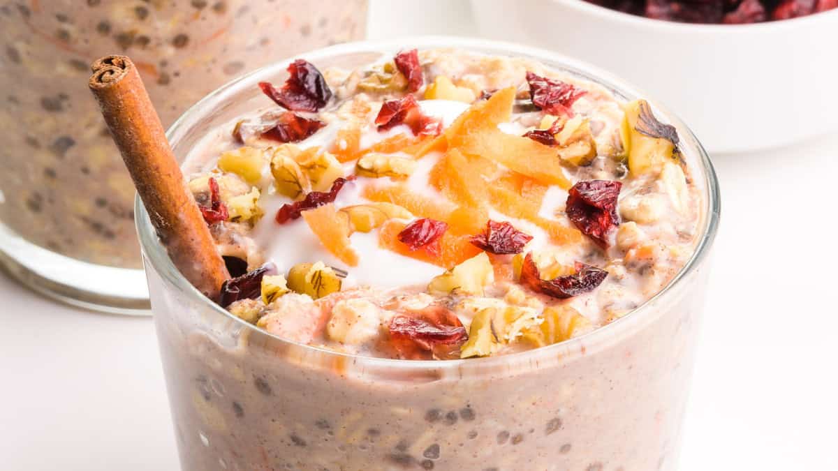 A glass jar filled with carrot cake overnight oats, including grated carrots, oats, raisins, and a cinnamon stick.