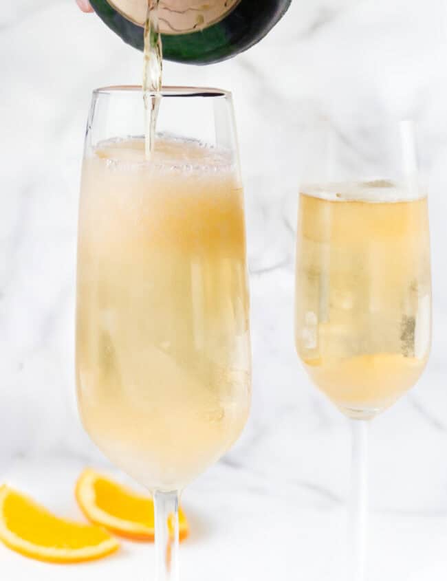 A person pouring champagne from a bottle into a flute glass.