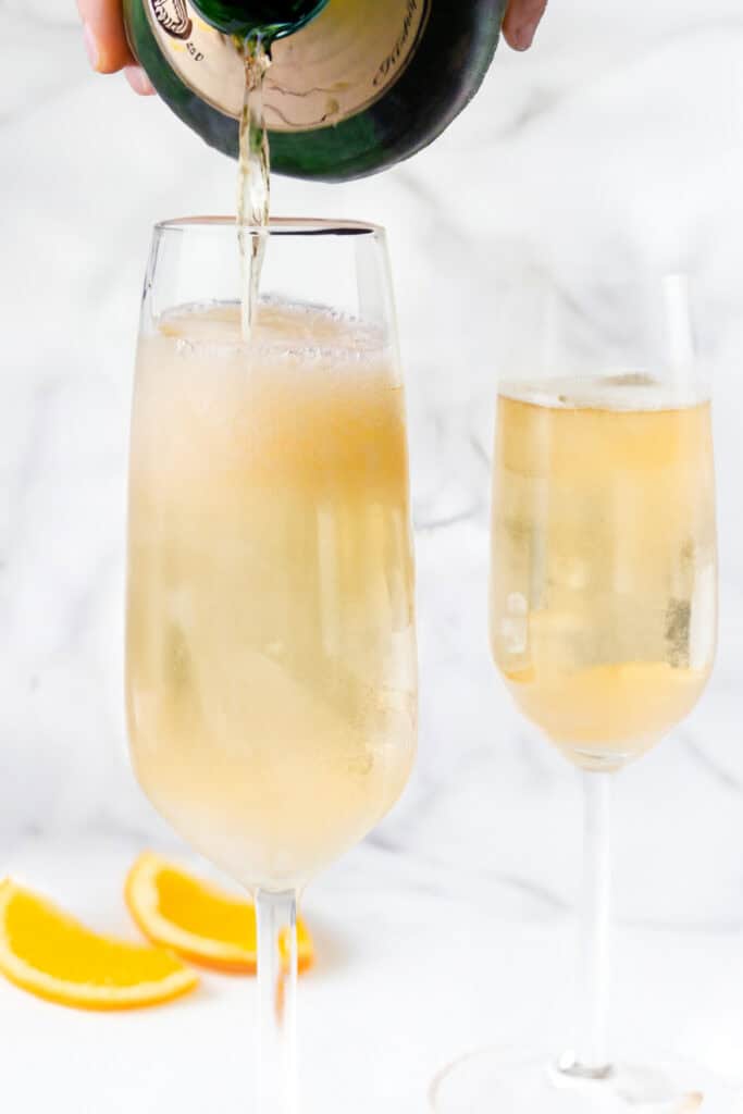 A person pouring champagne from a bottle into a flute glass.