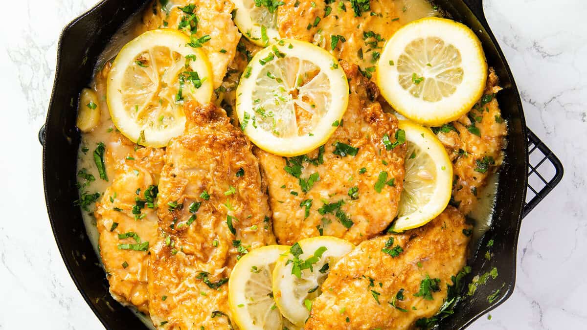 a close up image of Chicken Francaise in a black pan.