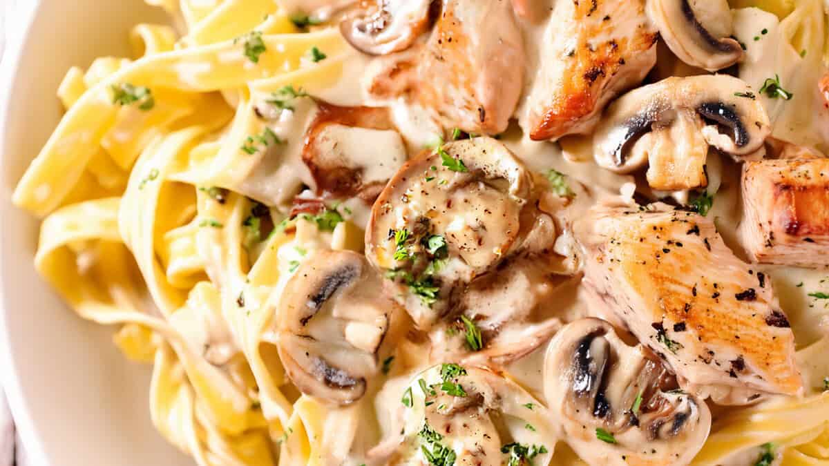 a close up image of chicken and mushroom fettuccine alfredo on a white plate.