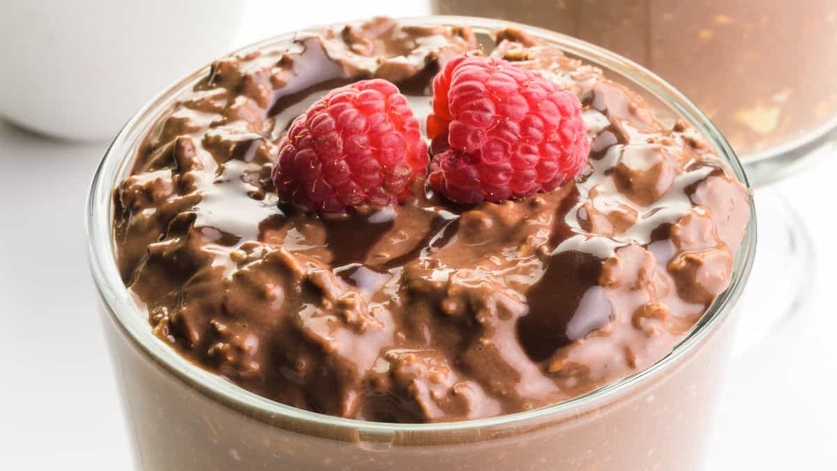 A glass jar filled with chocolate overnight oats, layered with fresh raspberries and drizzled with chocolate sauce.