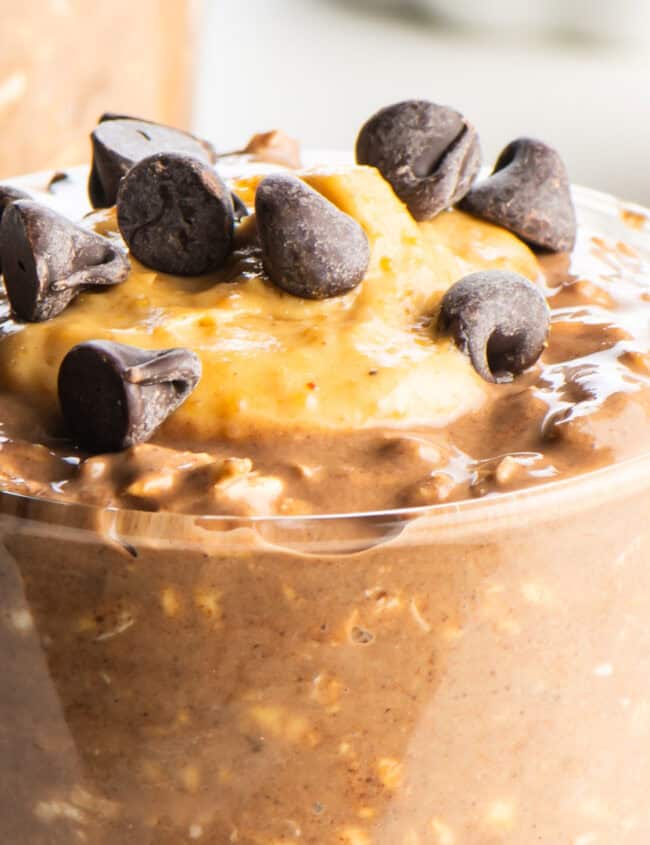 A glass jar layered with chocolate peanut butter overnight oats, featuring rolled oats, chocolate shavings, peanut butter swirls, and a drizzle of chocolate sauce.