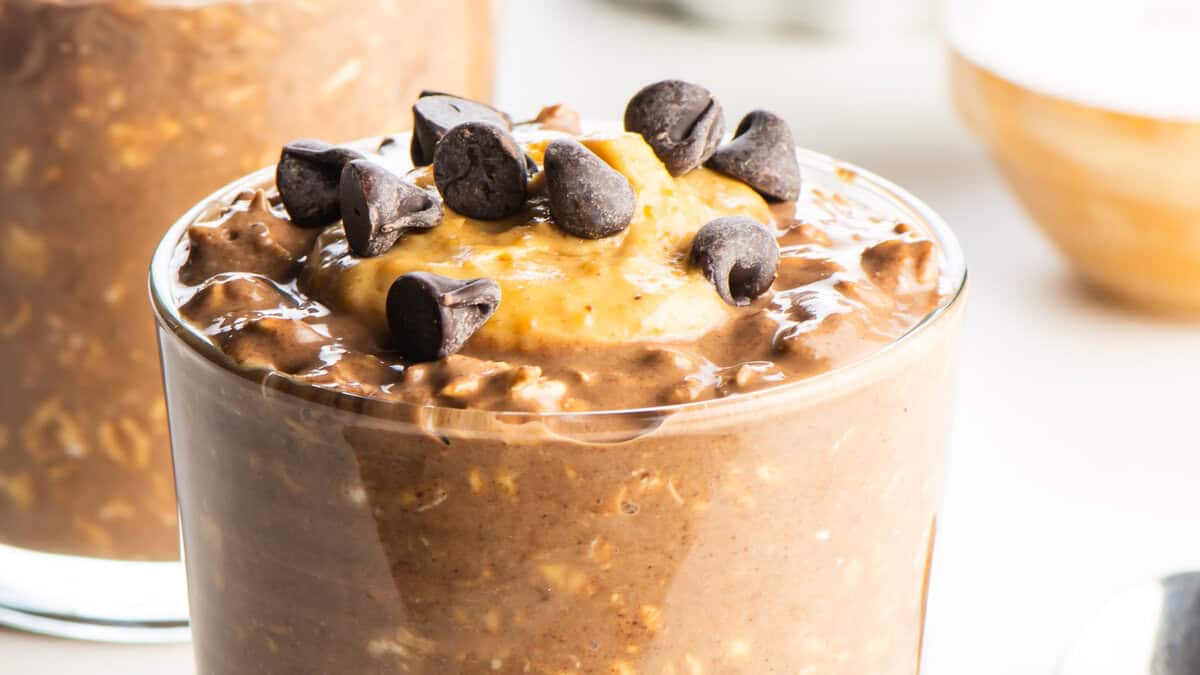 A glass jar layered with chocolate peanut butter overnight oats, featuring rolled oats, chocolate shavings, peanut butter swirls, and a drizzle of chocolate sauce.