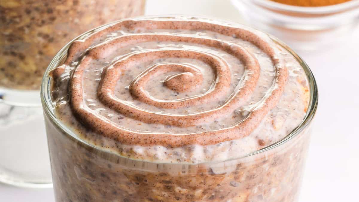 A glass jar filled with cinnamon roll overnight oats, layered with rolled oats, a brown sugar swirl, and a cinnamon crumble topping.