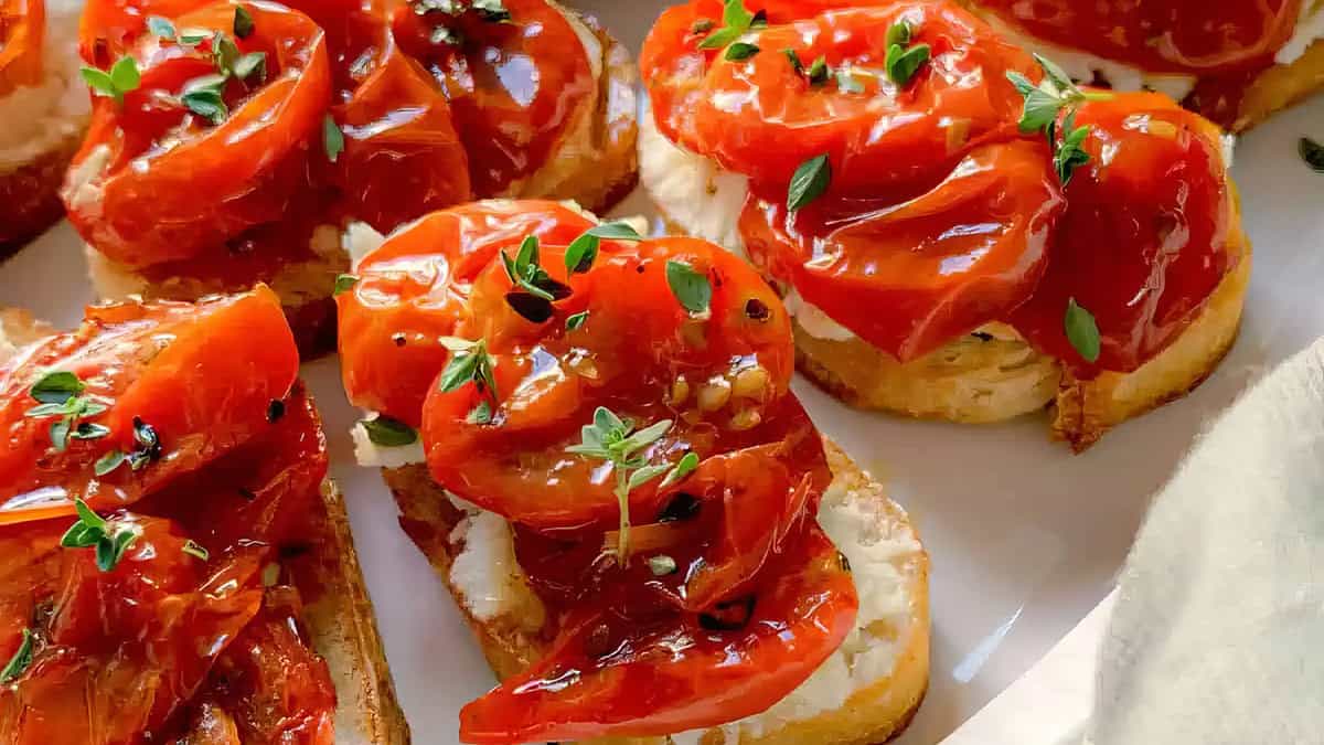 A close up image of vibrant Roasted Tomato Crostini on a white plate.