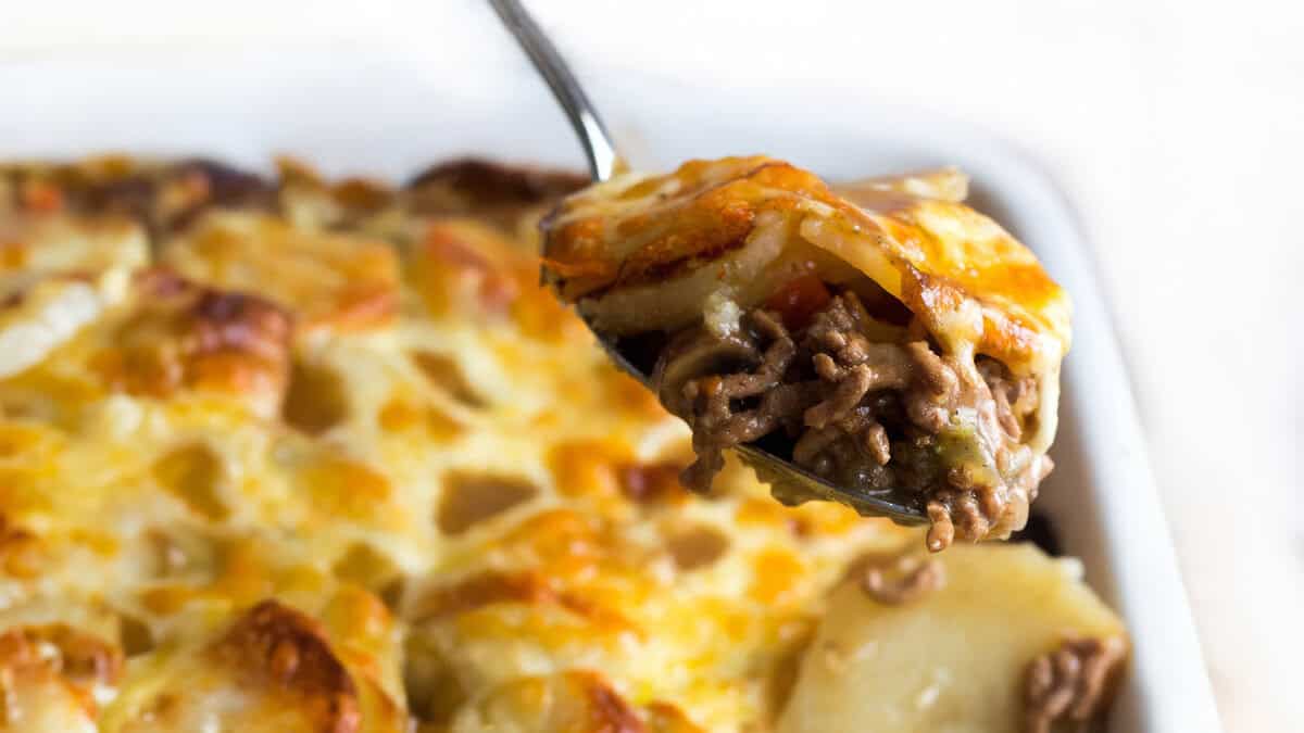 A spoon serving cottage pie stopped with cheesy potatoes.