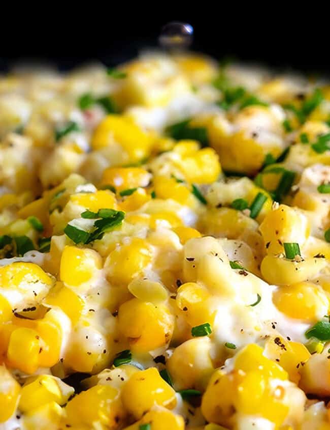 a close up image of cream cheese corn scattered with chopped fresh herbs.