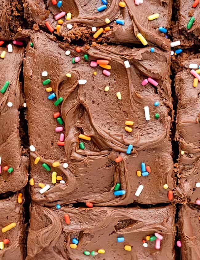 A close up image of a sliced cake with chocolate frosting and sprinkles.