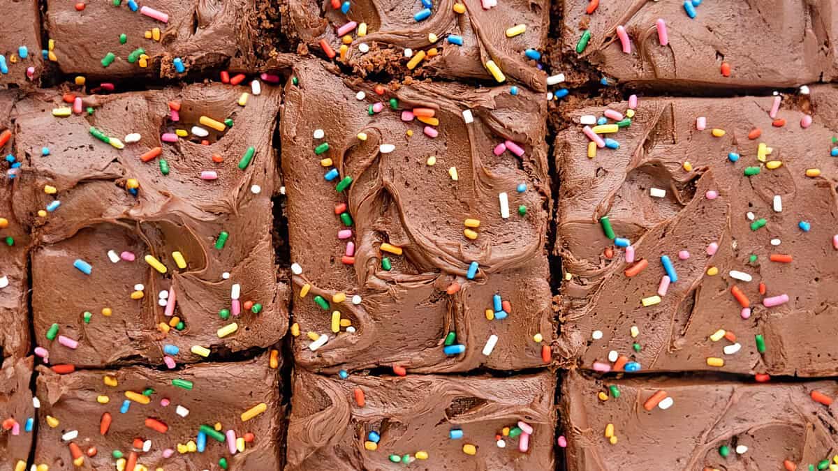 A close up image of a sliced cake with chocolate frosting and sprinkles.