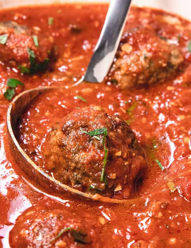 Meatballs in sauce being served with a spoon.