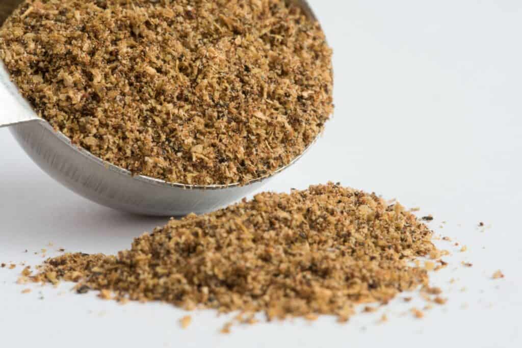 A close up image of a tablespoon of Garam Masala with some spilled out onto a table.