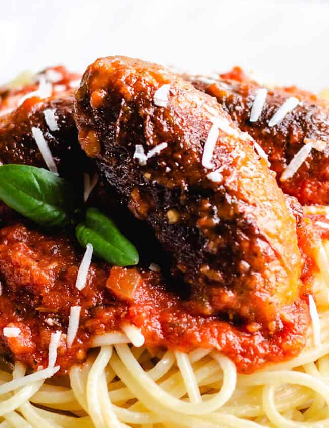 Spaghetti and Italian Sausage with a block of cheese and grater in the background.