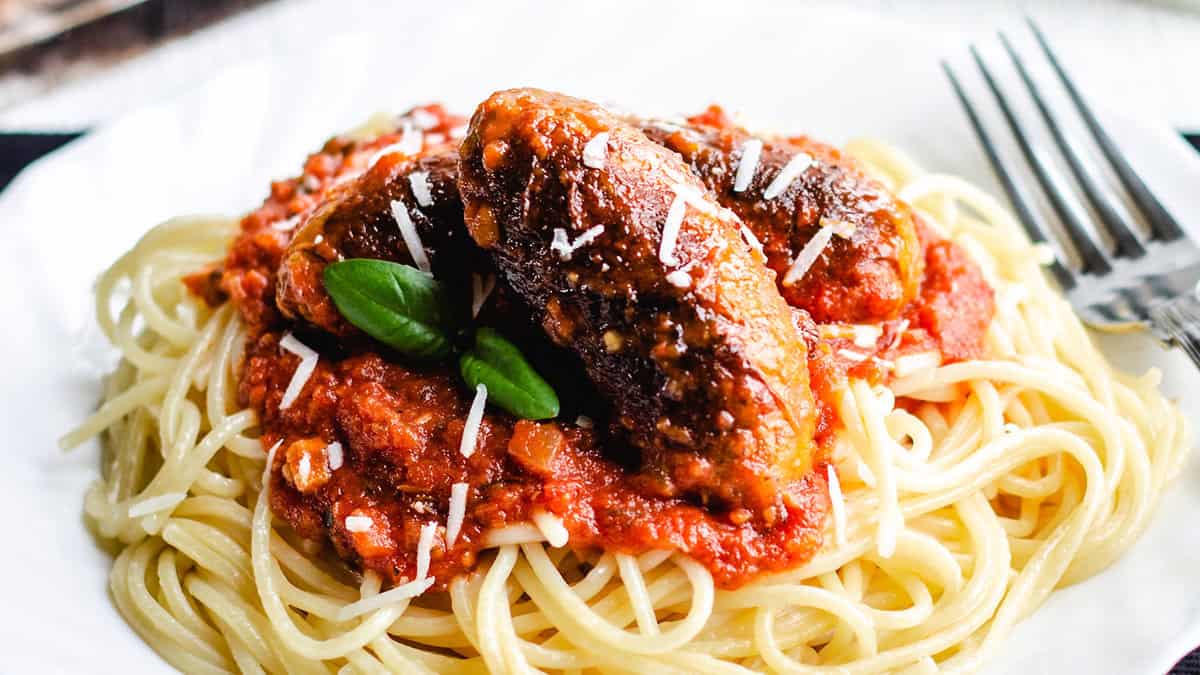 Spaghetti and Italian Sausage with a block of cheese and grater in the background.