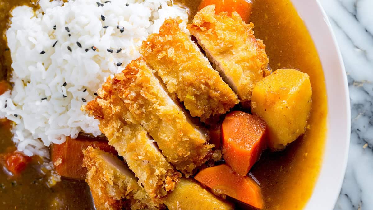 A close up image of Katsu Curry over rice in a white bowl.