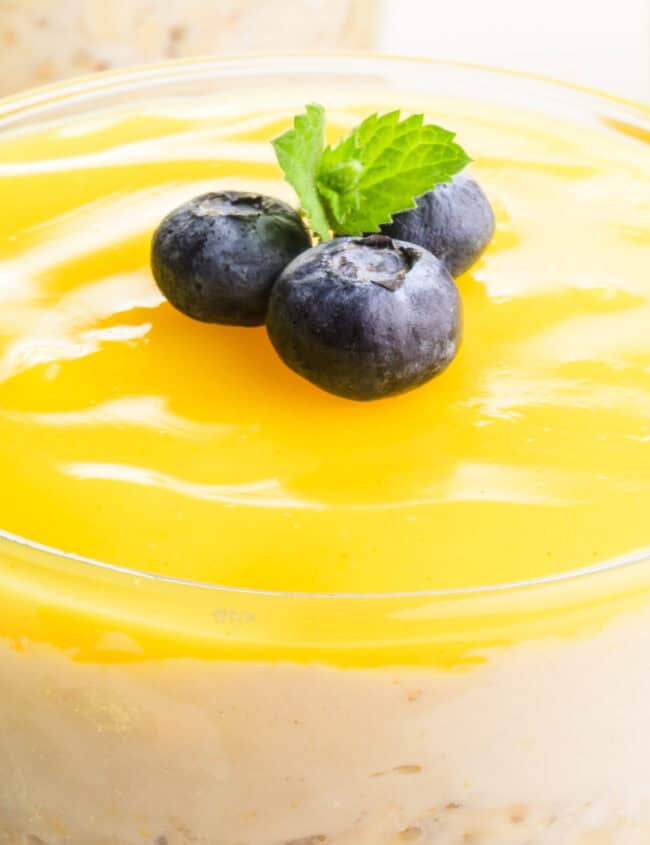 A close-up view of a glass jar filled with layered overnight oats. The oats appear to be yellow and include lemon slices and chia seeds.