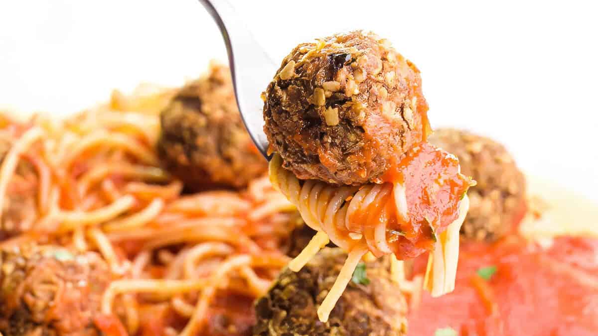 A close up image of spaghetti and lentil meatballs on a fork.