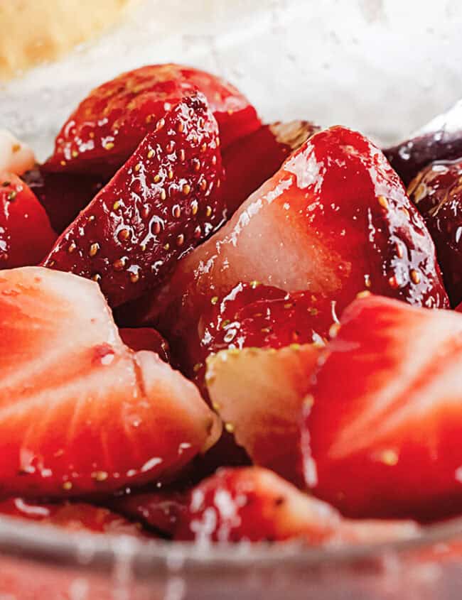 Close up of sliced strawberries in clear glass bowl glazed with sugar. Spoon in bowl.