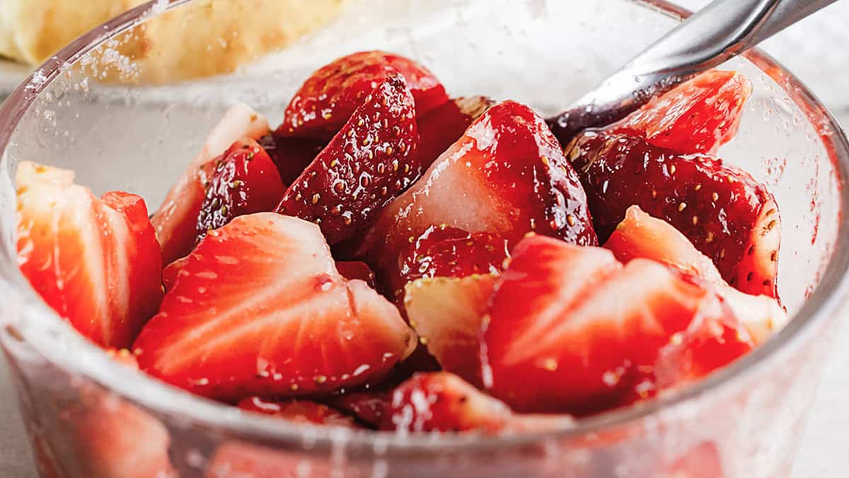 Close up of sliced strawberries in clear glass bowl glazed with sugar.  Spoon in bowl.