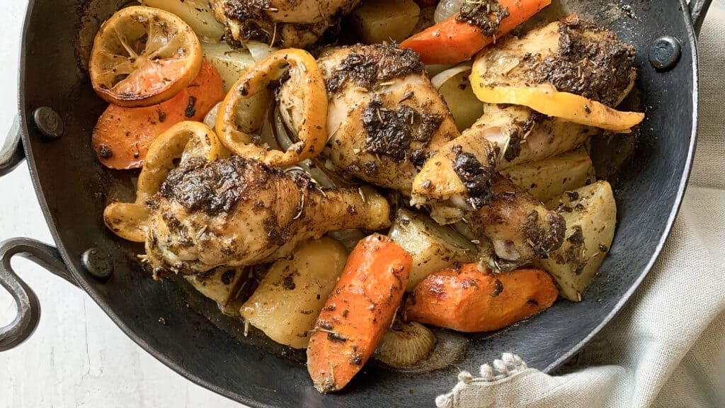 A close up image of a pan with cooked chicken, carrots and potatoes.