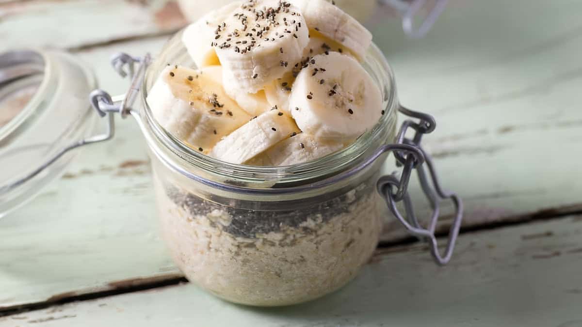 A glass jar filled with overnight oatmeal, layered with sliced bananas, chia seeds, and rolled oats