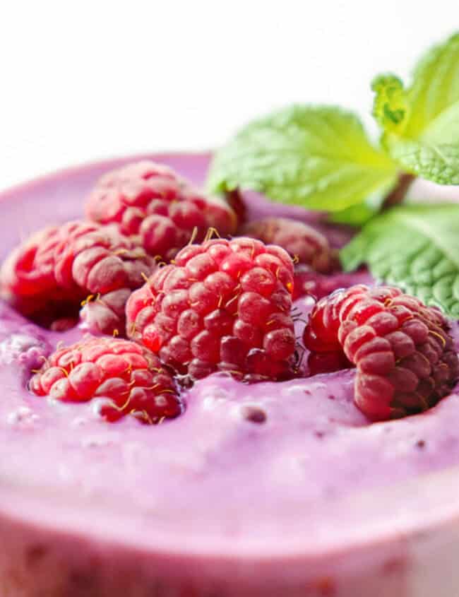 A glass of raspberry smoothie with raspberries and mint.