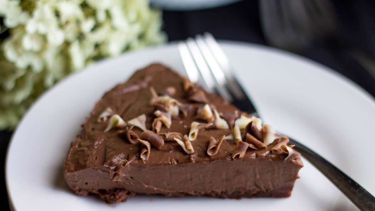 A close up image of a Chocolate Torte on a white plate with a dark background.